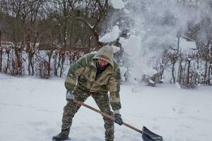 hombre borra el yarda de nieve con pala. pesado nevada en invierno. alto nivel de nieve. Nevado ventisquero. foto