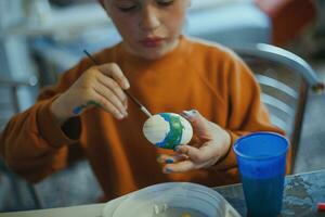 A child decorates an Easter egg in the colors of the rainbow. A child holds an egg and paints it with a brush. Preparing for the celebration of Easter. photo