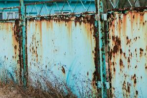 un oxidado cerca a un abandonado recurso en el playa. cerca con un agrietado azul pintar foto