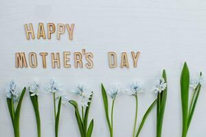 HAPPY MOTHERS DAY wording wooden letters on white background. row of spring flowers Scilla siberica at bottom. flat lay. Top view. photo