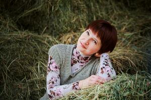 A young girl sits on a haystack propping her head on her palm. A rural woman rests after a day's work. photo