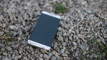 Smartphone with broken display lies on ground with stones photo