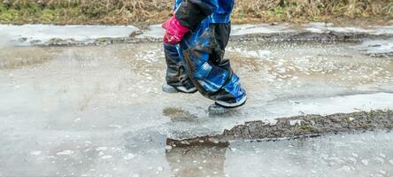 A child in a winter jumpsuit on ice on the road in the spring during the thaw. photo