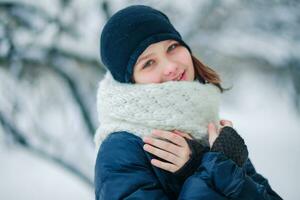 A young girl in a long white scarf on a background of snow-covered branches of trees in the city. photo