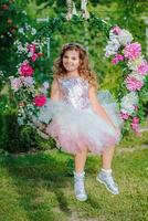 Beautiful little girl of preschool age in delicate dress sitting on a swing decorated with flowers . photo