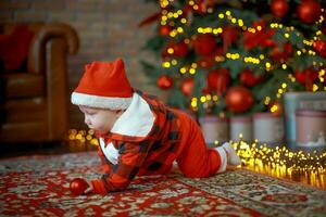 Little surprised child in santa costume in festive room on Christmas eve. Girl on background of Christmas tree. photo