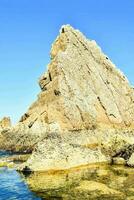 a rock formation in the ocean with clear water photo