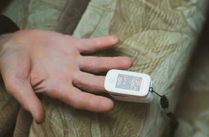 pulse oximeter is placed on index finger of old man hand to measure saturation. Close-up. Prevention and diagnosis of pneumonia. photo