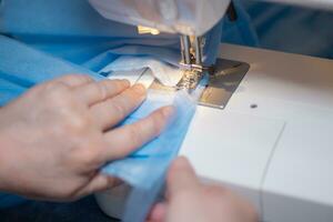 Sewing Homemade protective medical mask in process. woman holds a spunbond, sms, Meltblown mask at home. Detail White modern sewing machine and three-layer masks. photo