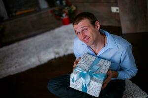 A young man holding a box with a gift. Sitting on wooden floor n photo