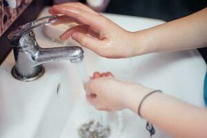 child closes the faucet with flowing water. Saving water. Hand washing to protect against the coronavirus virus. photo