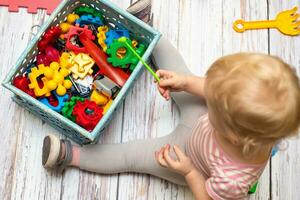 pequeño caja lleno con para niños pequeño juguetes para educación. ver desde cima. pequeño niño se sienta cerca caja de desarrollando juguetes juguetes revestimientos son multicolor. formas color reconocimiento forma juguetes con vistoso clasificador foto