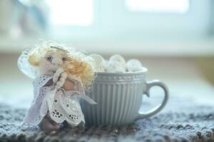 angel in white lace dress with hands folded in prayer. homemade sock toy with fluffy red hair in background of window. cup of marshmallows on knitted napkin. photo