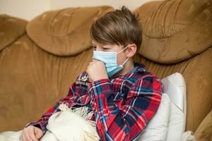 boy in protective medical mask lies in bed and coughs. Kid child is sick. child with influenza or cold protected from viruses among patients with coronavirus. photo