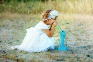 A little girl sitting on the sand near a large lantern. photo