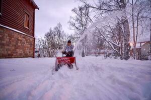 un joven hombre borra nieve con un nieve soplador en su patio trasero. foto