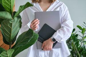 A woman holds a laptop and graphics tablet against a background of greenery. photo