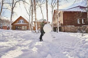 un familia construye un monigote de nieve fuera de blanco nieve en el yarda en invierno. foto
