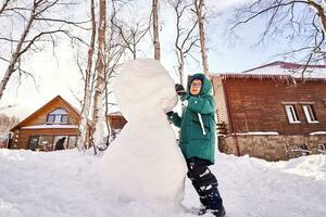 un familia construye un monigote de nieve fuera de blanco nieve en el yarda en invierno. foto