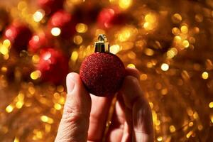 New Year's red ball in a woman's hand on golden tinsel. photo