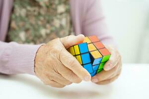 Bangkok, Thailand - May 15, 2022 Asian elderly woman playing Rubik cube game for treatment dementia prevention and Alzheimer disease. photo