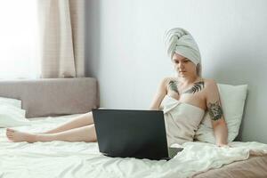 Tver, Russia-august 2, 2021. A tattooed woman after a shower is lying on the couch with a laptop. photo