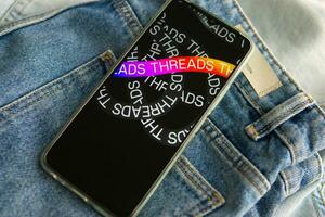 Tver, Russia - July 15, 2023, the threads logo on the smartphone screen lying on the jeans. The threads icon. The logo of the current application. Threads social network. photo