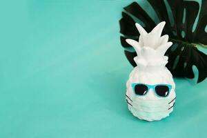 Pineapple in a medical mask and sunglasses on a blue background. Summer concept. Summer in Covid-19. Vision for the summer of 2021 during the coronavirus pandemic. photo