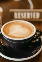 Coffee cup with a heart pattern in a blue cup on a wooden background. A sign with the inscription - reserved. photo