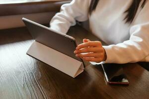 A girl at a wooden table in a restaurant is working on a tablet. Women's hands close-up. photo