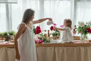 A little blonde girl with her mom on a kitchen countertop decorated with peonies. The concept of the relationship between mother and daughter. Spring atmosphere. photo