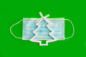 Christmas decorations decorative background. Decorative Christmas tree on a medical mask on a green background top View, minimalism, flat layout. Christmas and New year 2020. The Age Of Coronavirus. photo
