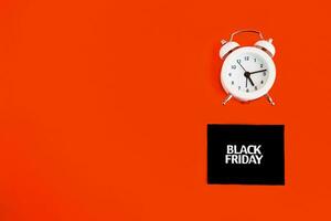 white alarm clock and an inscription on a black square - black Friday on a red background. The topic of sales. photo