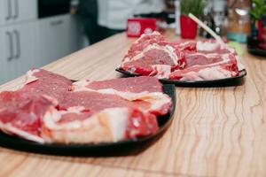 Raw beef meat for steak preparation. Raw beef sliced, preparation of meat for cooking steak at the culinary master class. Raw meat on a black plate. photo