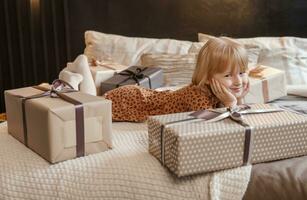 un pequeño rubia niña es acostado en un suave cama en un festivo interior decorado en un nuevo años estilo. el niño es esperando para un nuevo años regalo. foto