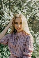 Blonde girl on a spring walk in the garden with cherry blossoms. Female portrait, close-up. A girl in a pink polka dot dress. photo