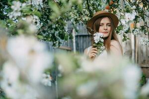 hermosa joven niña en blanco vestir y sombrero en floreciente manzana huerta. floreciente manzana arboles con blanco flores foto