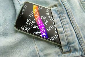 Tver, Russia - July 15, 2023, the threads logo on the smartphone screen lying on the jeans. The threads icon. The logo of the current application. Threads social network. photo