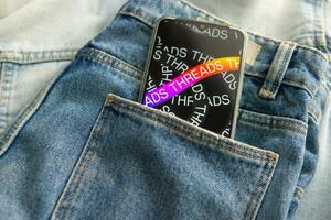 Tver, Russia - July 15, 2023, the threads logo on the smartphone screen lying on the jeans. The threads icon. The logo of the current application. Threads social network. photo