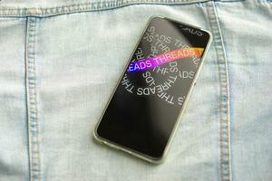 Tver, Russia - July 15, 2023, the threads logo on the smartphone screen lying on the jeans. The threads icon. The logo of the current application. Threads social network. photo