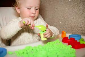 bebé sostiene molde para jugando con arena a hogar. educativo juguetes para niños arriba a año. niña obras de teatro con cinético arena. niño construye pastores en formar de letras de arena. temprano desarrollo de niños. foto