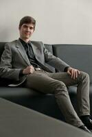 Handsome young man in suit sitting on couch in reception. Business man waiting for meeting. photo