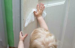 baby washes the vintage old doors with napkin during a viral epidemic. Cleaning home. Teaching children to be independent. use of wet wipes in everyday life photo