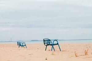 Lonely benches in an abandoned village in the area of hostilities in Ukraine. View from the Sea of Azov to Mariupol. Smoking chimneys by the sea. Ecological catastrophy. war in Ukraine. photo