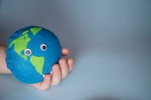 small child holds Earth. palm of child with thimble of felt in form of planet. Saving Ecology with children. Cosept Earth Day.World ocean day, saving water campaign photo