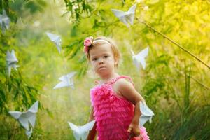 niño cerca papel mariposas pequeño niña en el arbustos iluminado por puesta de sol rayos foto