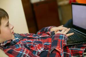 boy in plaid shirt does lessons on laptop. child learns remotely during quarantine of coronavirus. Online learning from home. photo