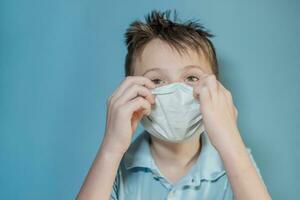 boy adjusts protective medical mask on face. Mistakes in dressing the mask. child touches face and carries virus. child with influenza or cold protected from viruses among patients with coronavirus photo