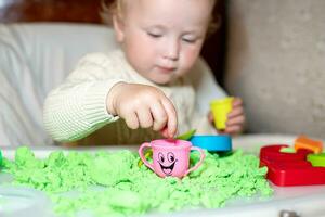 niña obras de teatro con cinético arena. niño construye pastores en formar de letras de arena. temprano desarrollo de niños. multa motor habilidades de el dedos. foto