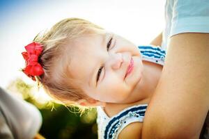 el pequeño niña en el brazos de madre sonriente calurosamente el bebé arrugado su ojos con placer. un niño con corto blanco cabello. foto